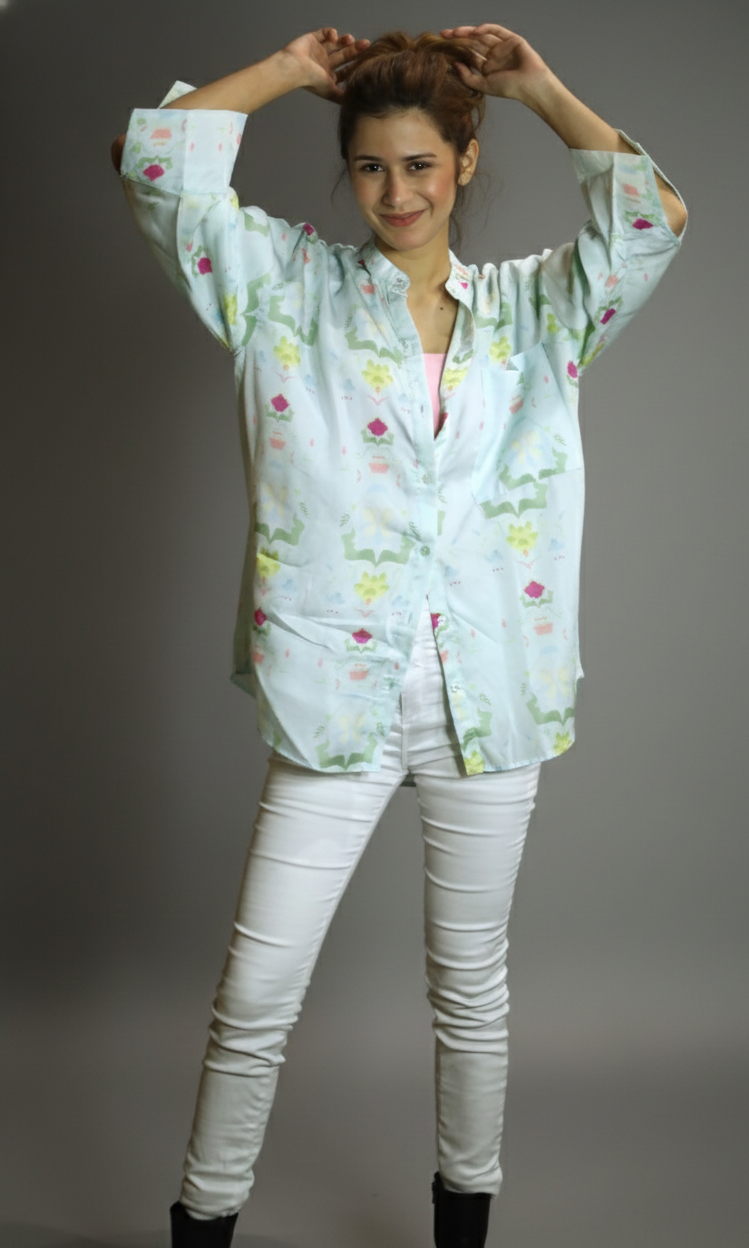 Woman wearing a light-colored floral blouse and white pants against a gray background