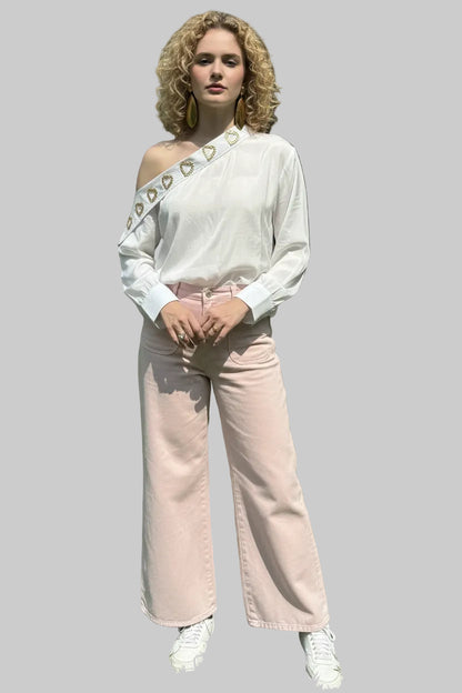 Woman wearing a white off-shoulder top with heart details and light pink pants outdoors.