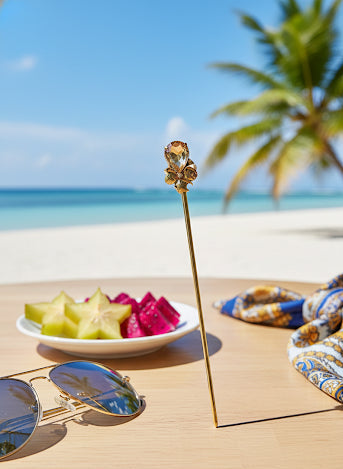 Sunglasses, fruit plate, and decorative item on a table with a beach and palm tree in the background