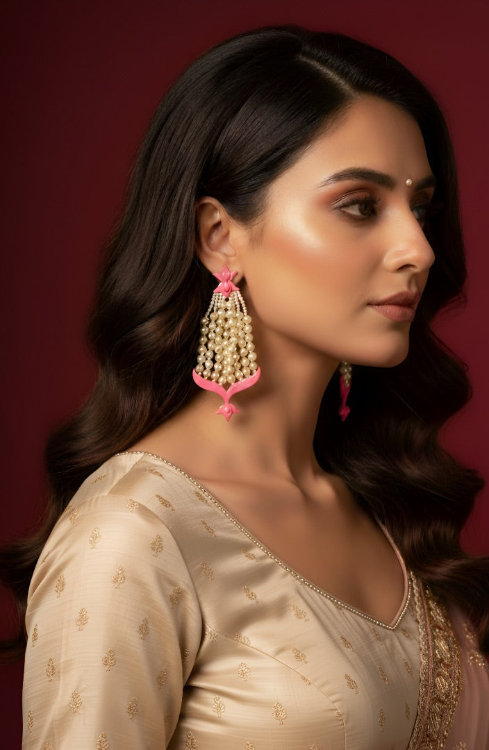 Woman wearing a beige saree with gold details and pink earrings against a red background