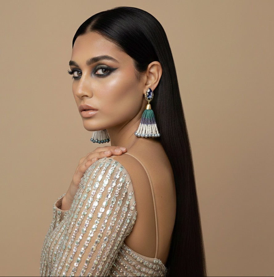 Woman wearing a beaded top and tassel earrings against a beige background