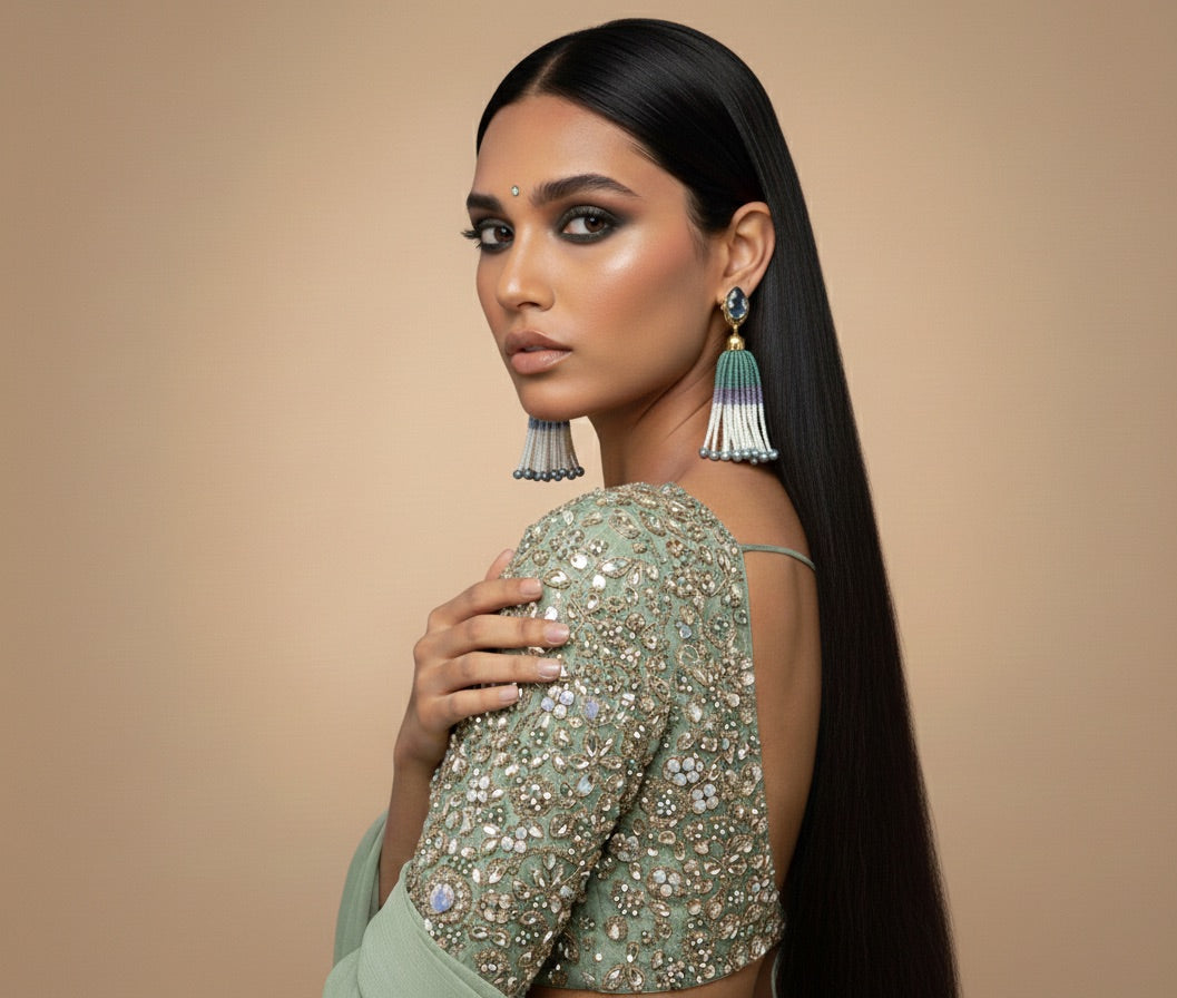 Woman wearing a green saree with intricate patterns and jewelry against a beige background