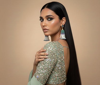 Woman wearing a green saree with intricate patterns and jewelry against a beige background