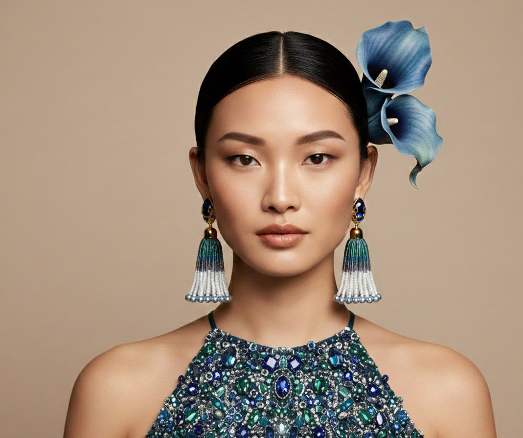 Woman wearing a beaded necklace and earrings with a blue flower in her hair against a beige background