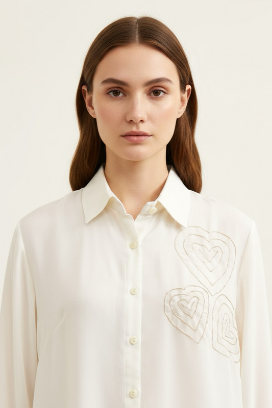 Woman wearing a white blouse with intricate embroidery on a plain background